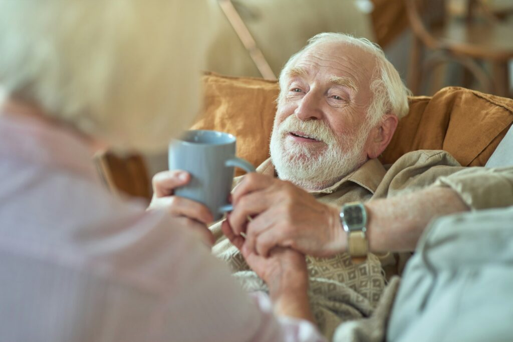 Careful senior lady giving cup of tea for her husband